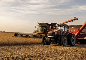 Agricultural combine harvester and red tractor working in a field.