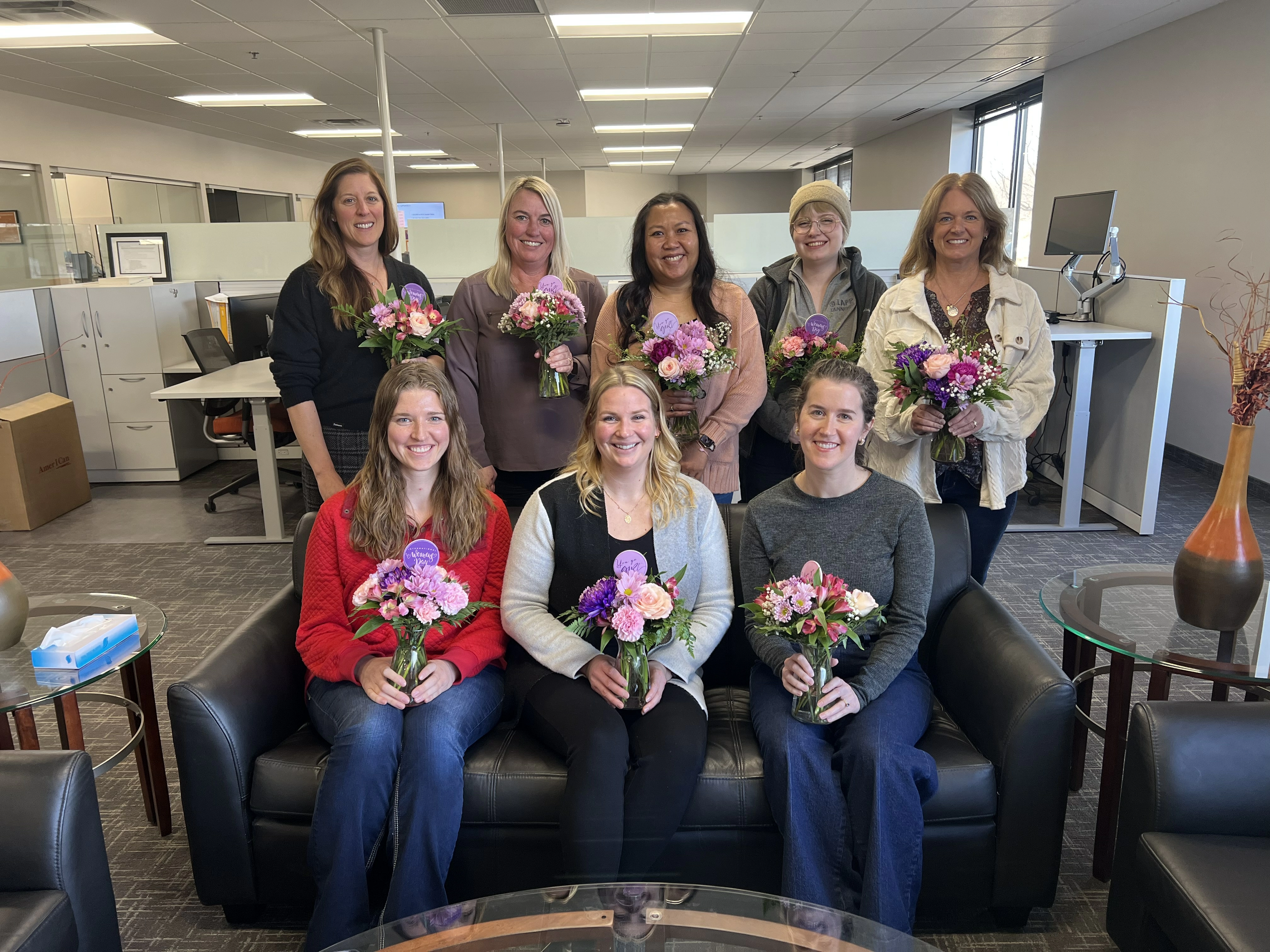 Employees posing and holding flowers they received for International Women's Day