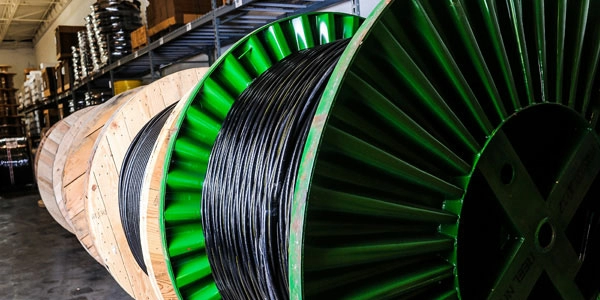 Black medium voltage cable on a large green spool inside a warehouse.